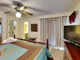 Quarto com cama, ventoinha no teto, televisão e janela com cortinas.
