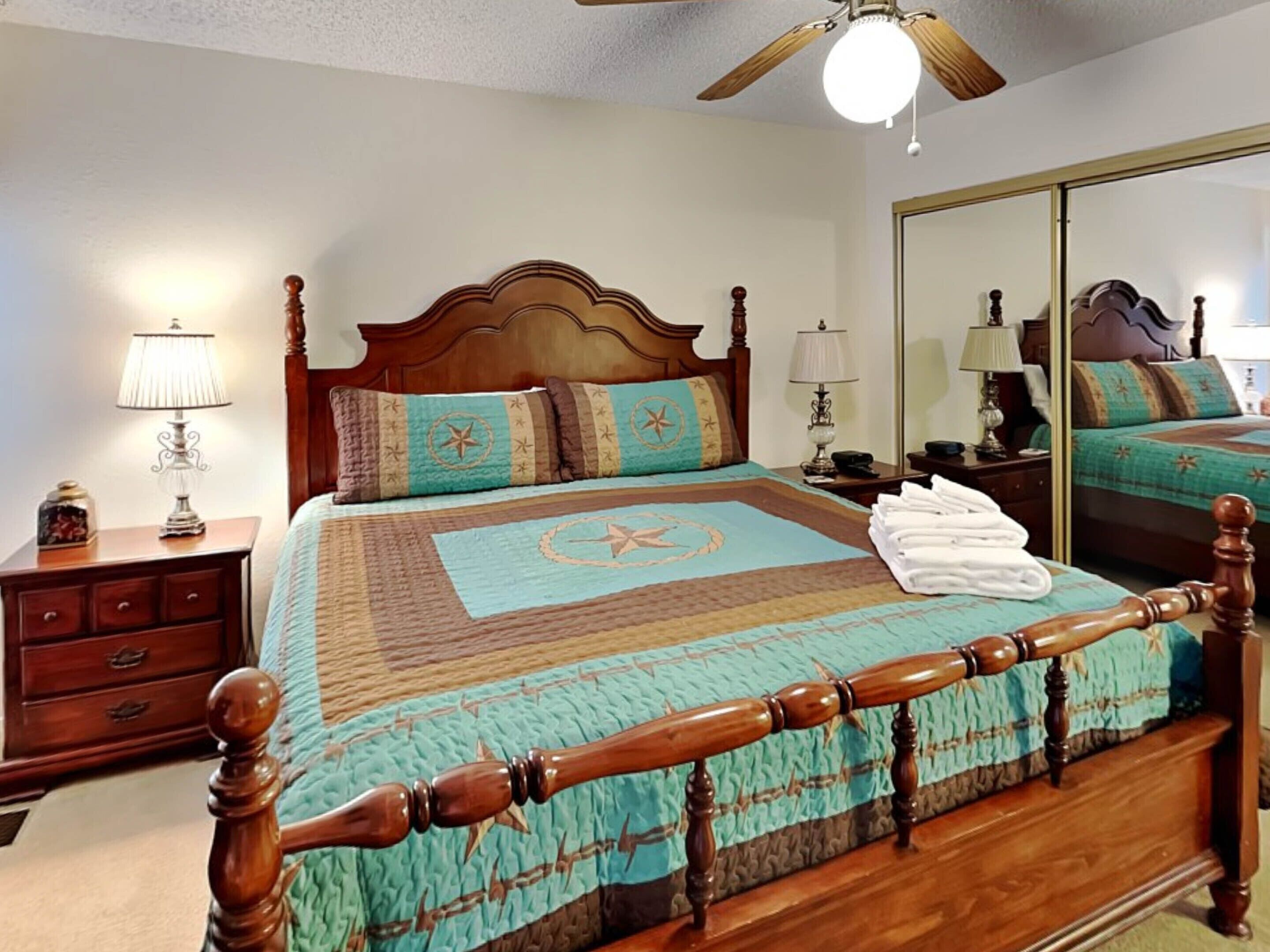 A neatly arranged bedroom with a wooden bed, a nightstand, a lamp, and a mirror.