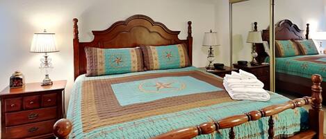 A neatly arranged bedroom with a wooden bed, a nightstand, a lamp, and a mirror.