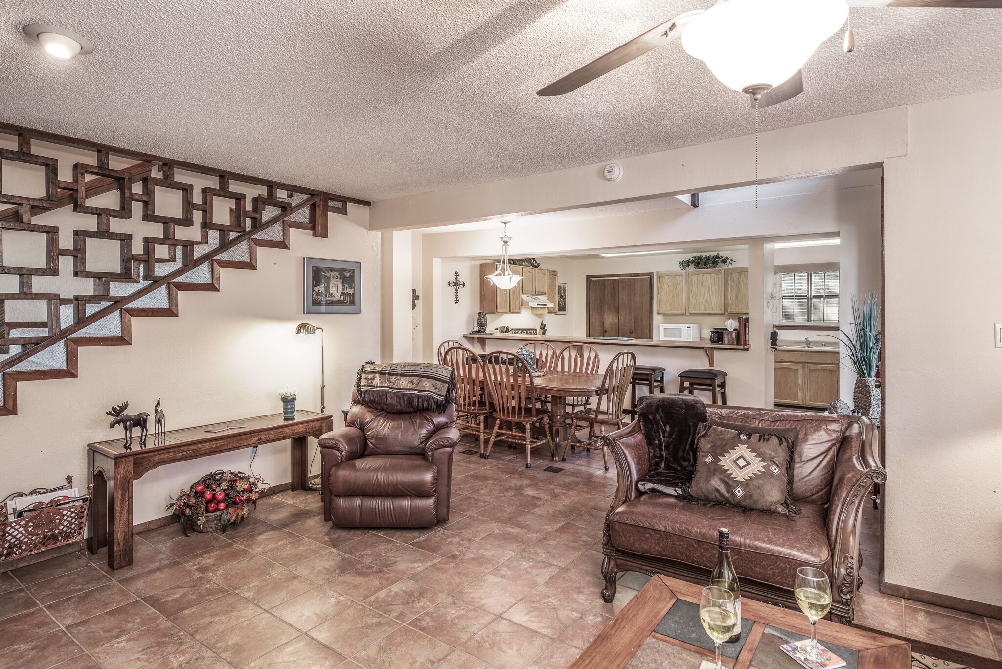 A spacious living area with a wooden staircase, leather furniture, a dining table, and a kitchen in the background.
