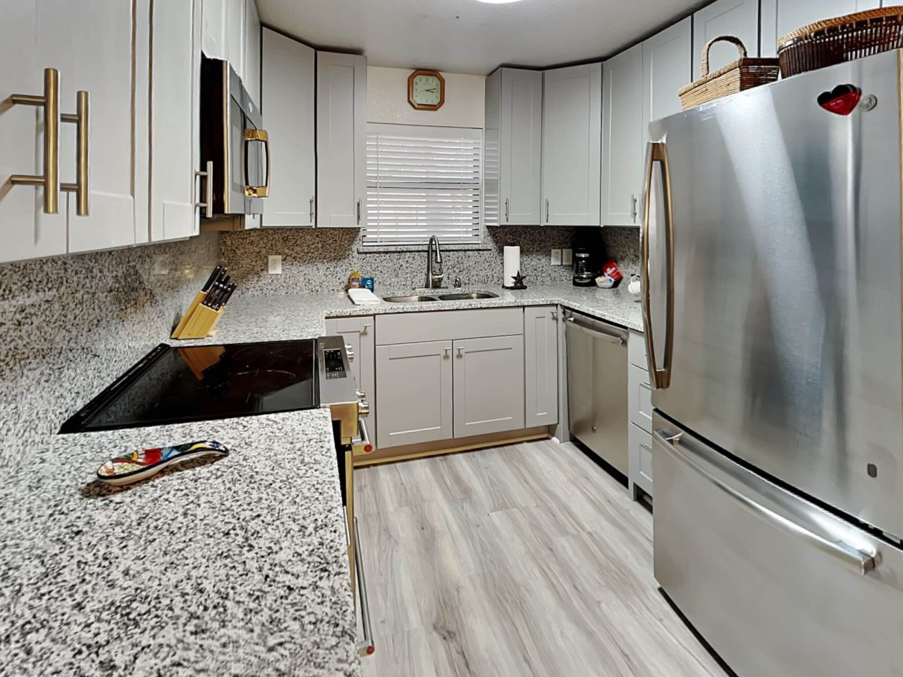 A modern kitchen with white cabinets, a stainless steel refrigerator, a built-in oven, and a granite countertop.