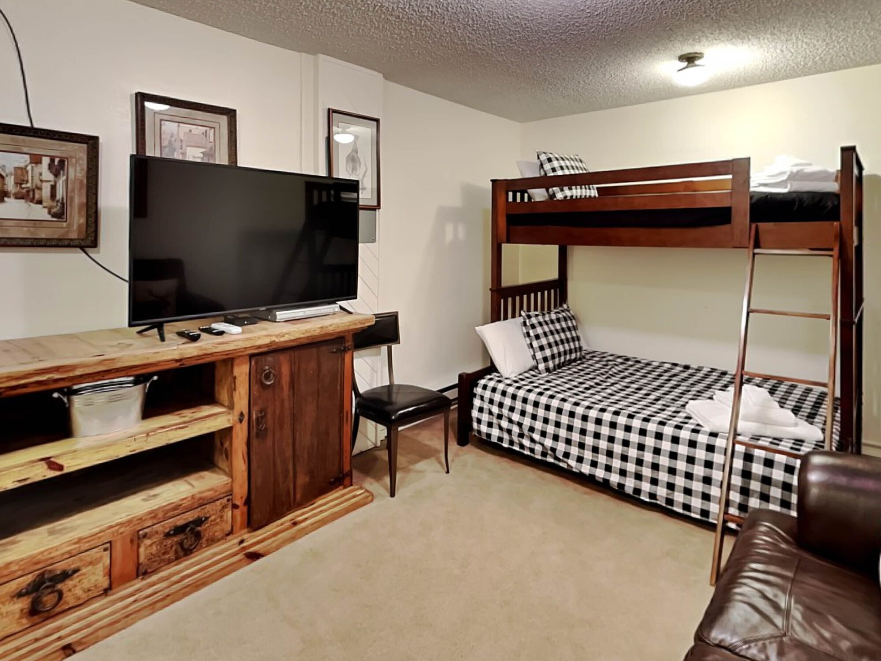 Een kamer met een stapelbed, een houten bureau en een televisie, plus een stoel.
