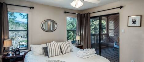 A bedroom with a bed, a ceiling fan, a window with curtains, a bedside table with a lamp, and a tray with breakfast items.