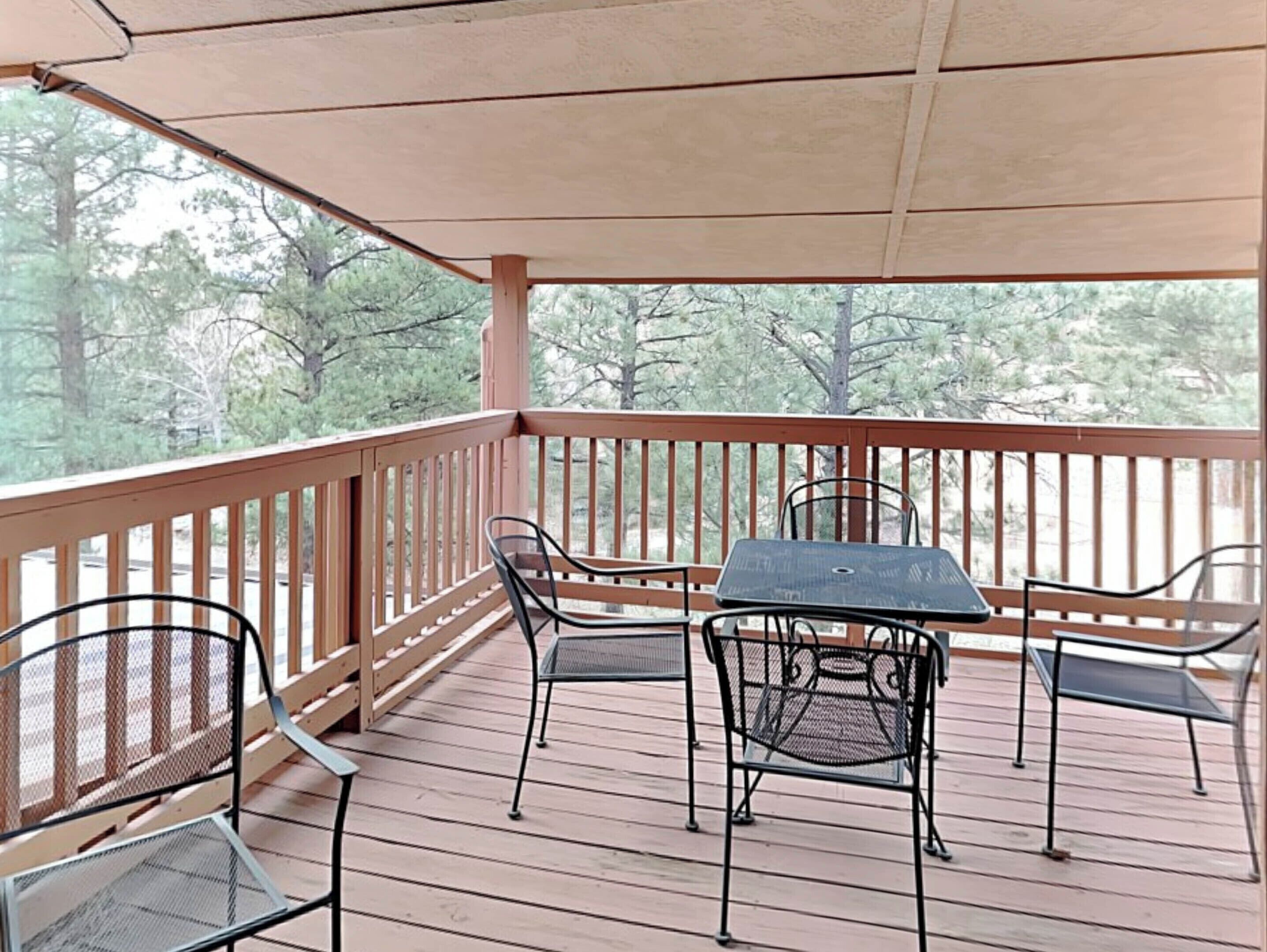 A covered outdoor deck with a table and chairs, surrounded by a wooden railing.