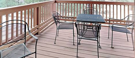 A covered outdoor deck with a table and chairs, surrounded by a wooden railing.