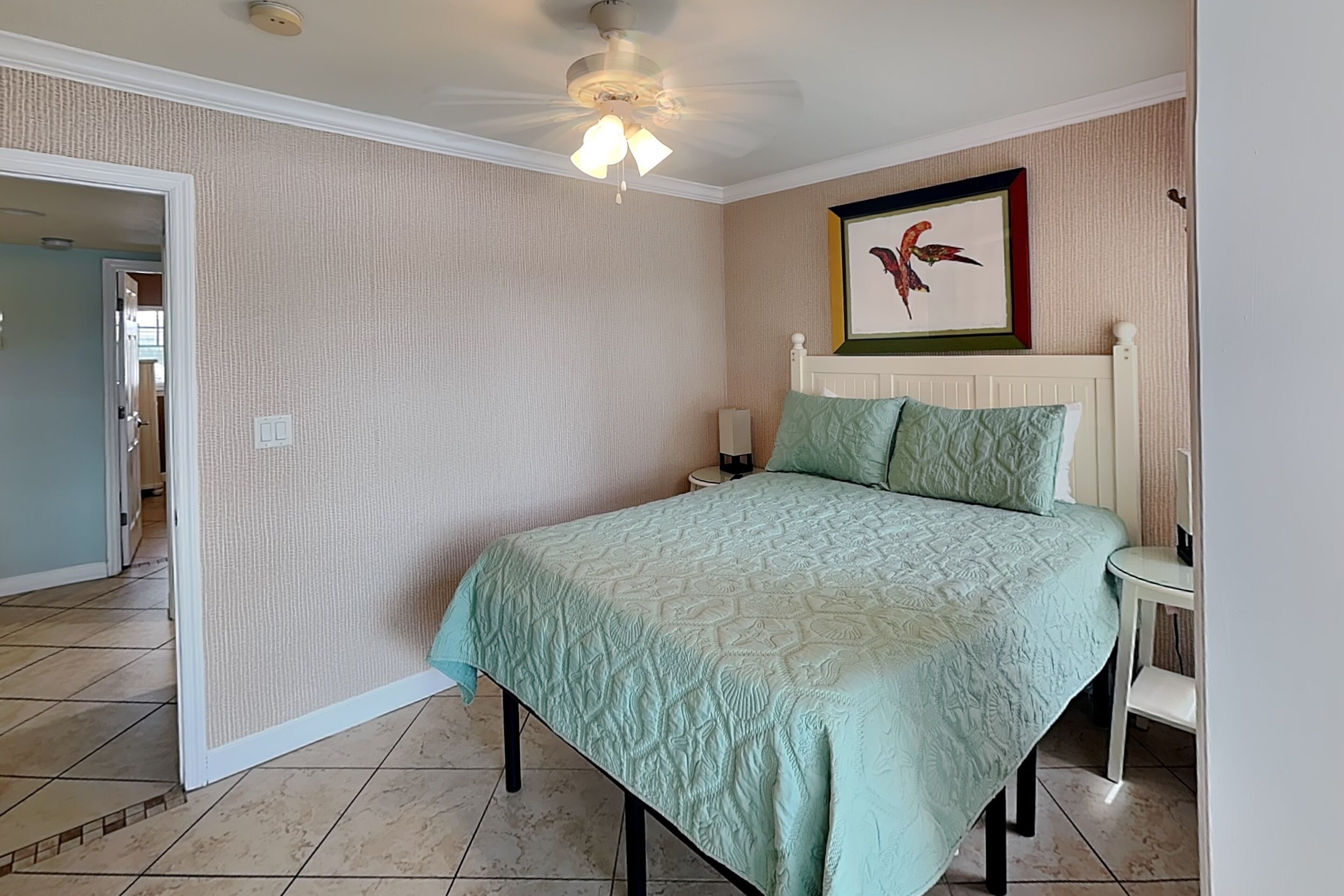 A bedroom with a bed, a nightstand, a framed picture, and a ceiling fan.