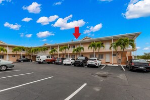 A hotel with a parking lot, multiple cars, and a clear blue sky with clouds. - Bare Foot A212 by Distinctive Beach Rentals (Indian Shores)