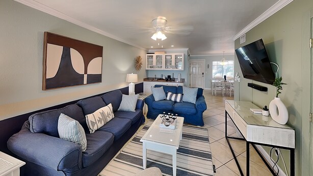 A living room with a sofa, coffee table, and TV. There is a kitchen in the background.