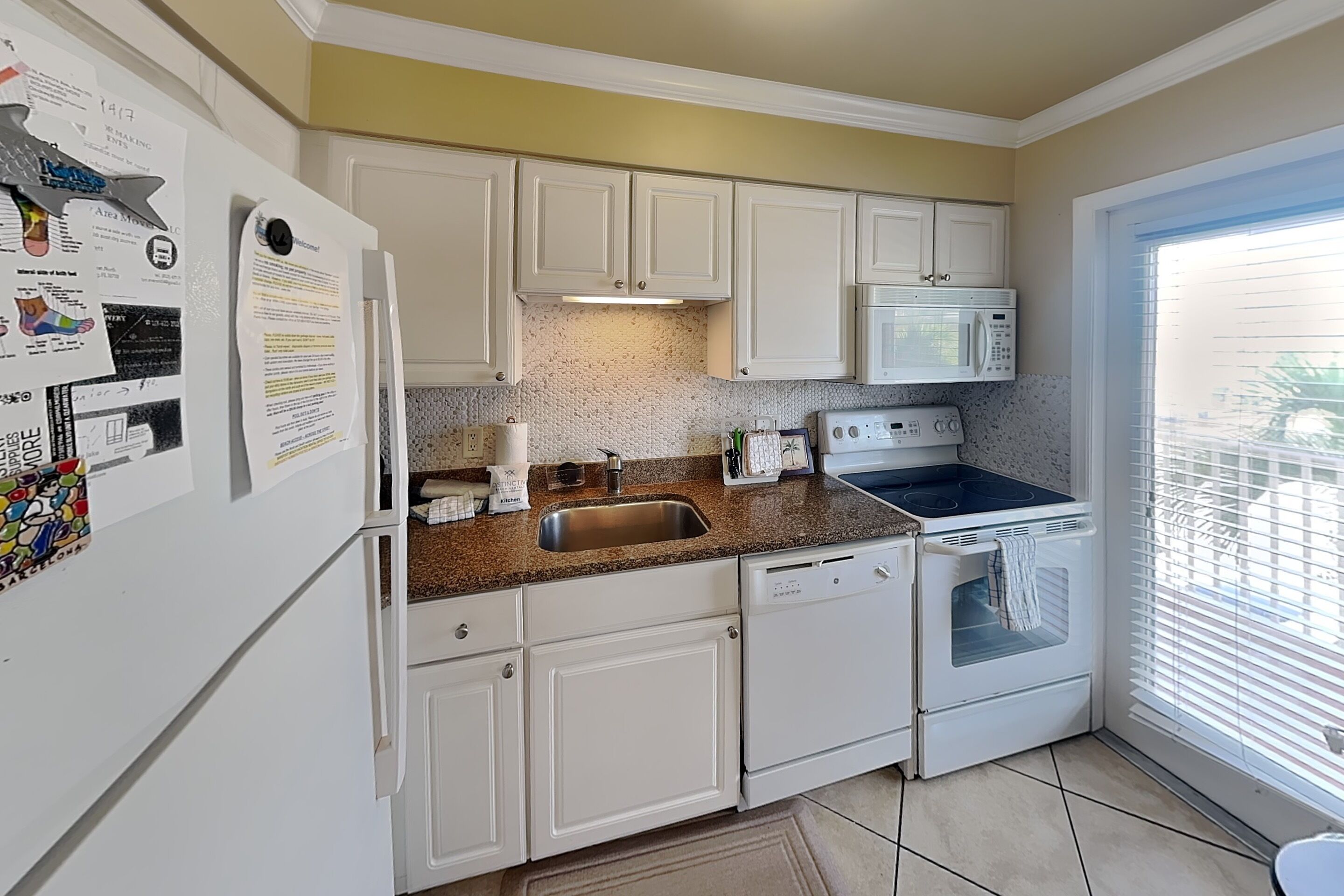 A kitchen with white cabinets, a stainless steel sink, a microwave, and an oven.