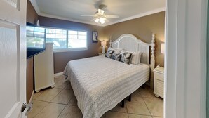 A bedroom with a bed, nightstands, a ceiling fan, a window, and a door.