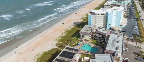Vista aérea de un hotel costero con playa, piscina y varios edificios.