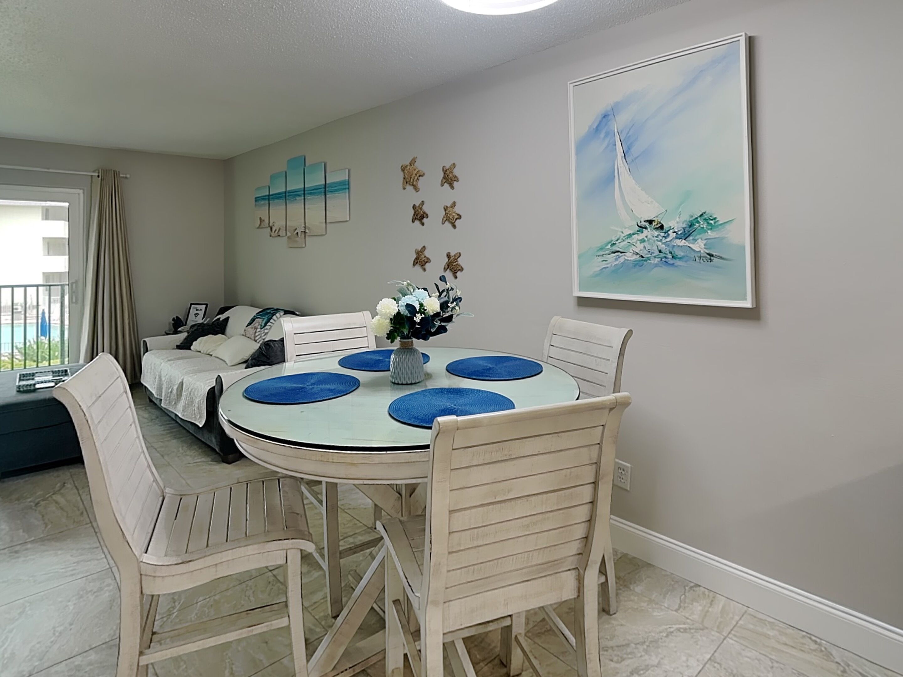 Un comedor con una mesa redonda, sillas blancas y un cuadro de un velero en la pared.