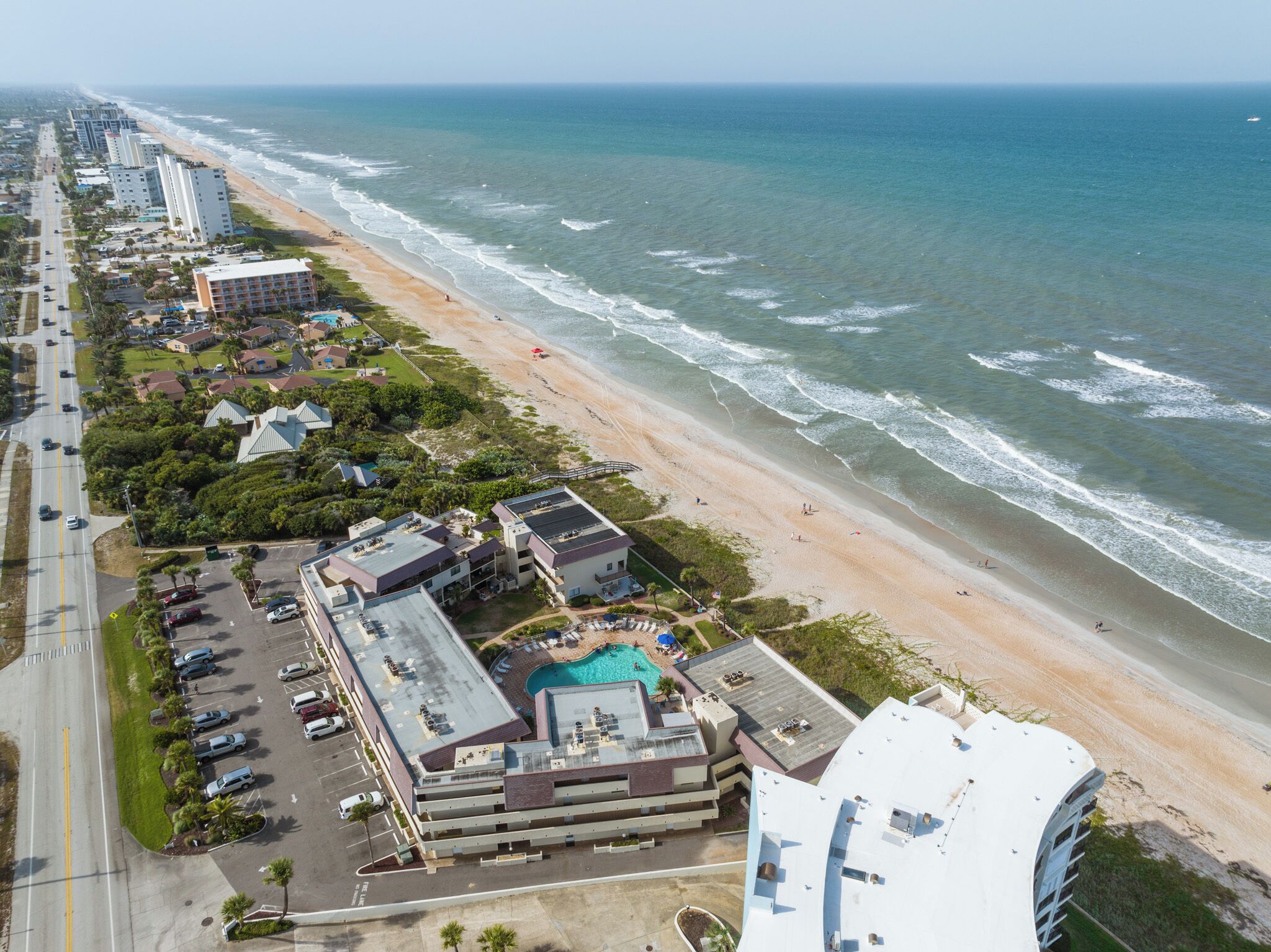 Luchtbeeld van een kusthotel met zwembad, toegang tot het strand en aangrenzende hoogbouw.