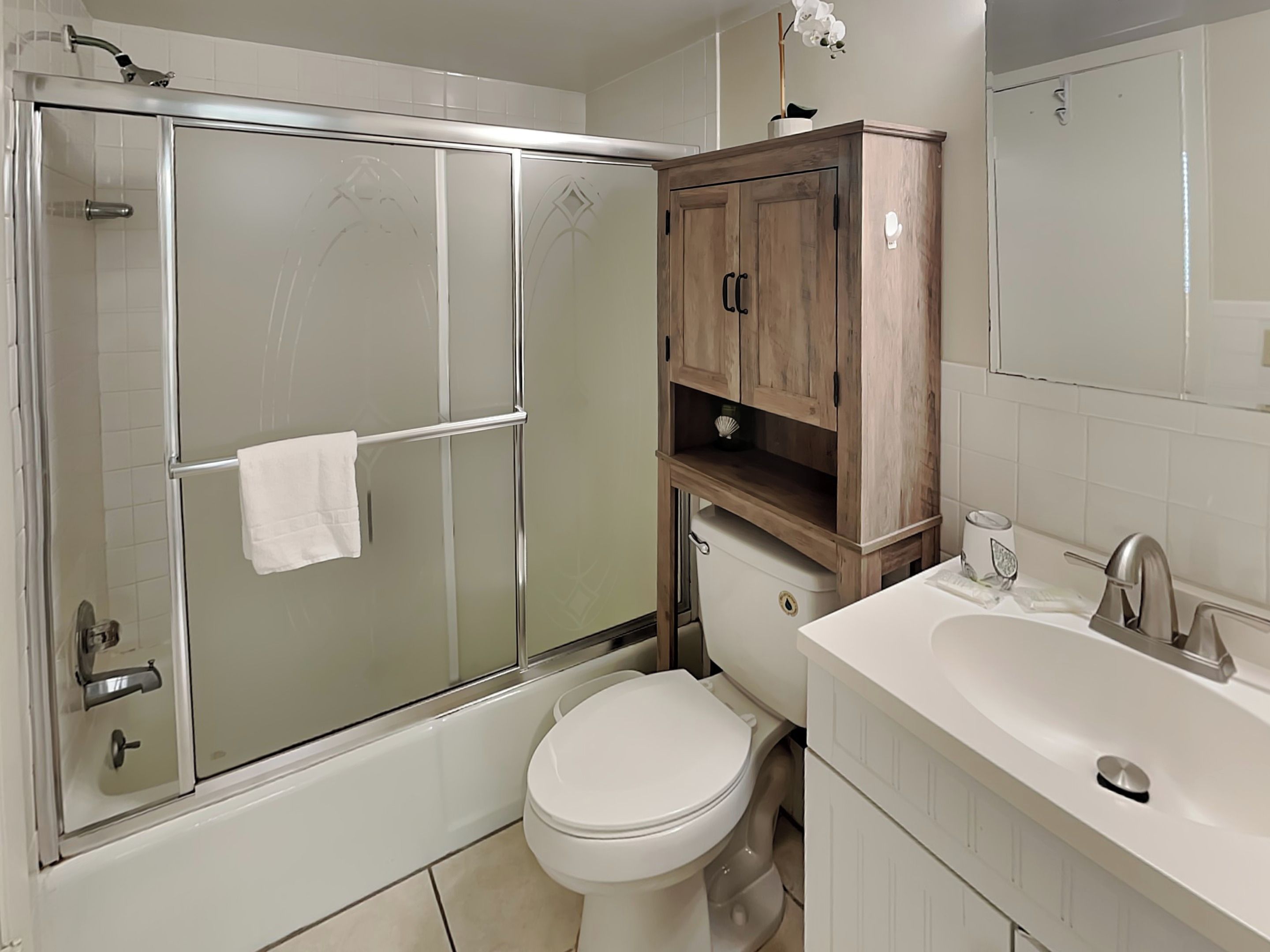 Une salle de bain moderne avec une douche à parois de verre, des toilettes blanches et un meuble en bois au-dessus du lavabo.