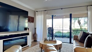 Un salon moderne doté d’un téléviseur à écran plat, de canapés en cuir, d’une table basse et d’une grande fenêtre donnant sur un paysage verdoyant.