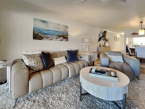 Un salon moderne avec un canapé beige, une table basse ronde et un tableau représentant une scène de plage.