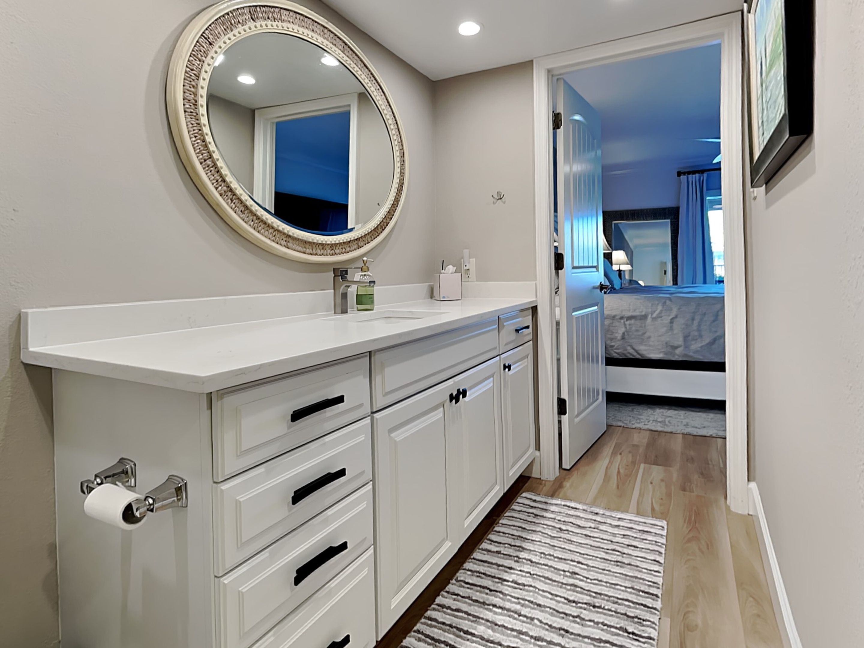 A modern bathroom with a large mirror, white cabinetry, and a wooden floor.