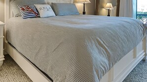 Une chambre à coucher avec un grand lit, deux lampes de chevet, un ventilateur de plafond et une fenêtre avec des rideaux.