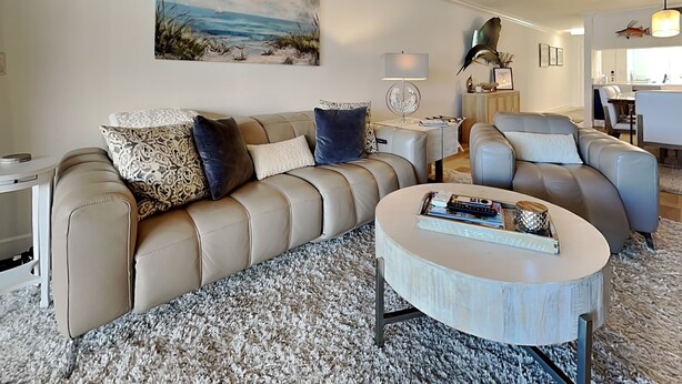 Un salon moderne avec un canap é beige, une table basse ronde et un tableau représentant une scène de plage.