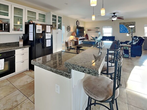 A modern kitchen with granite countertops, white cabinetry, and a central island with bar stools.