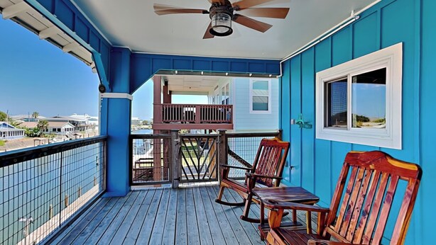 Eine Holzterrasse mit Deckenventilator, Geländer und Blick aufs Meer.