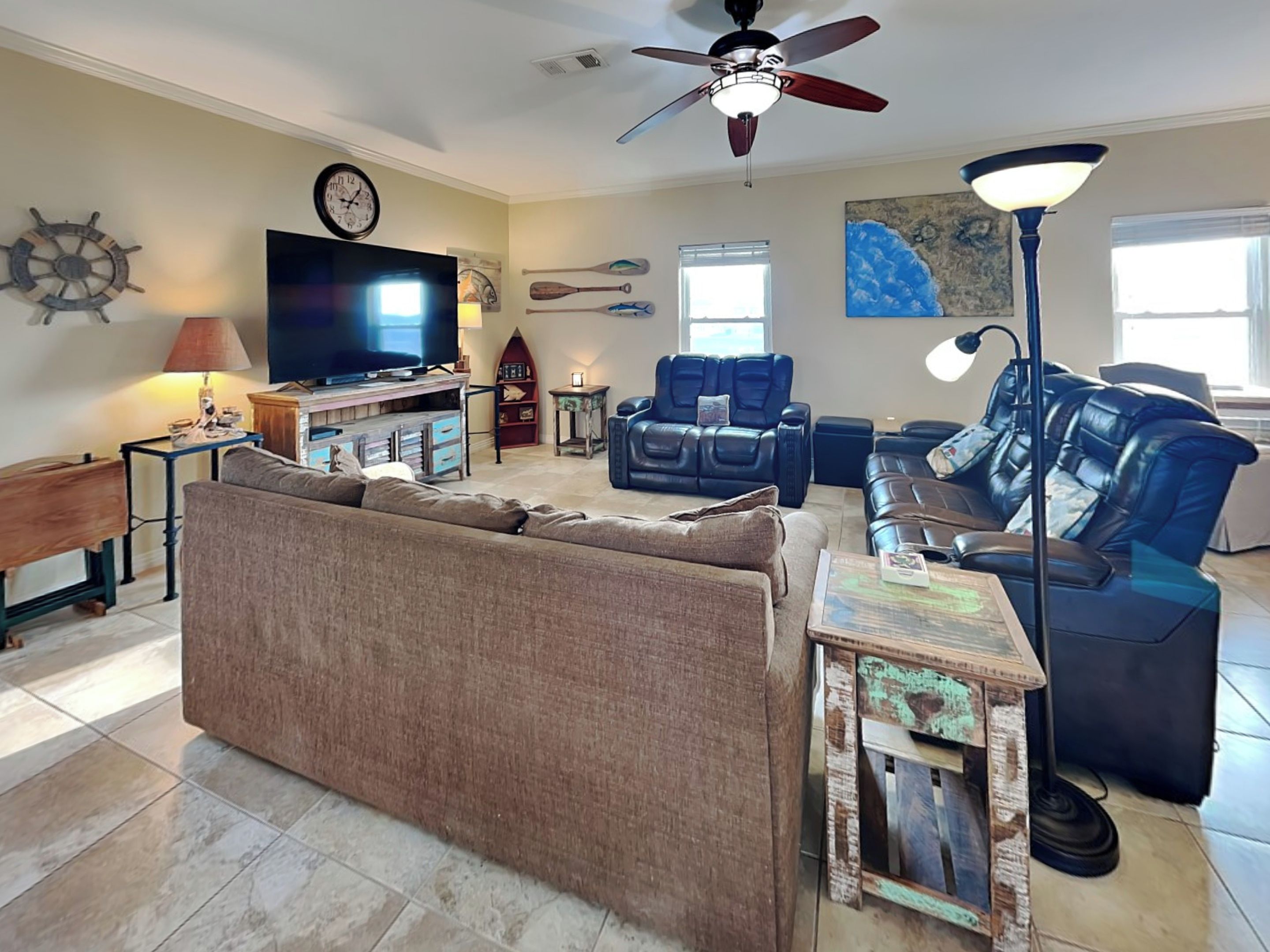 A living room with a sofa, a television, a ceiling fan, and a wall clock.