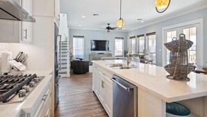 A modern kitchen with a central island, stainless steel appliances, and a large window. - Key West by Ryson Vacation Rentals (Galveston)