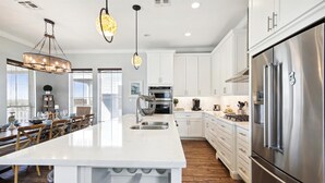 A modern kitchen with white cabinetry, stainless steel appliances, and a large island with wine storage. - Key West by Ryson Vacation Rentals (Galveston)
