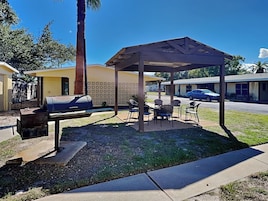 Un patio exterior con una parrilla, sillas y un área de estar techada.