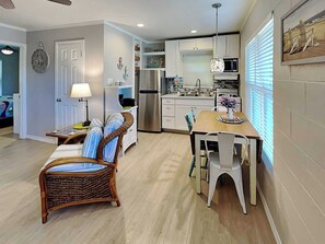 A modern kitchen with white cabinets, a stainless steel refrigerator, and a dining area with wicker chairs and a wooden table. - Harbor Lights Cottages #3 by Miss Kitty’s (Fulton)