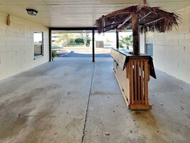 Uma área externa coberta com piso de concreto, um banco de madeira e uma estrutura de telhado de palha.