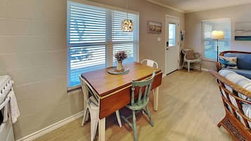 A dining area with a wooden table and chairs, a hanging lamp, and a view through the window.