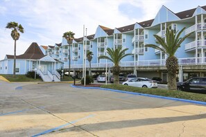 Un hôtel situé en bord de mer, doté de nombreux balcons, de palmiers et d’un espace de stationnement.