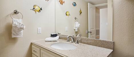 A bathroom with a sink, two towel rings, a mirror, and decorative fish wall art.