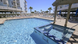 A pool area with clear blue water, lounge chairs, and a wooden pergola. - Abundant Relaxation by Ryson Vacation Rentals (Galveston)