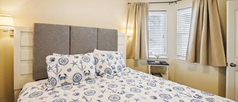 A bedroom with a bed, headboard, bedside lamps, curtains, and a window with blinds.