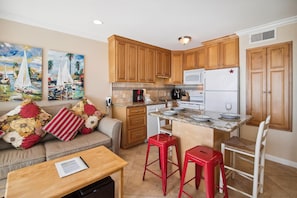 Una cocina compacta con armarios de madera, un refrigerador y un comedor con mesa y taburetes rojos.
