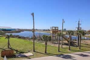Puisto, jossa on puinen rakennelma, palmuja, vesialue ja kirkas taivas.