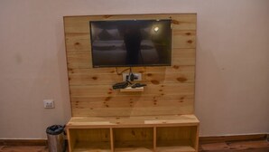 A wooden wall with a mounted flat-screen TV, a power outlet, and a trash bin. - The Tattwaa Corbett Spa & Resort (Ramnagar)
