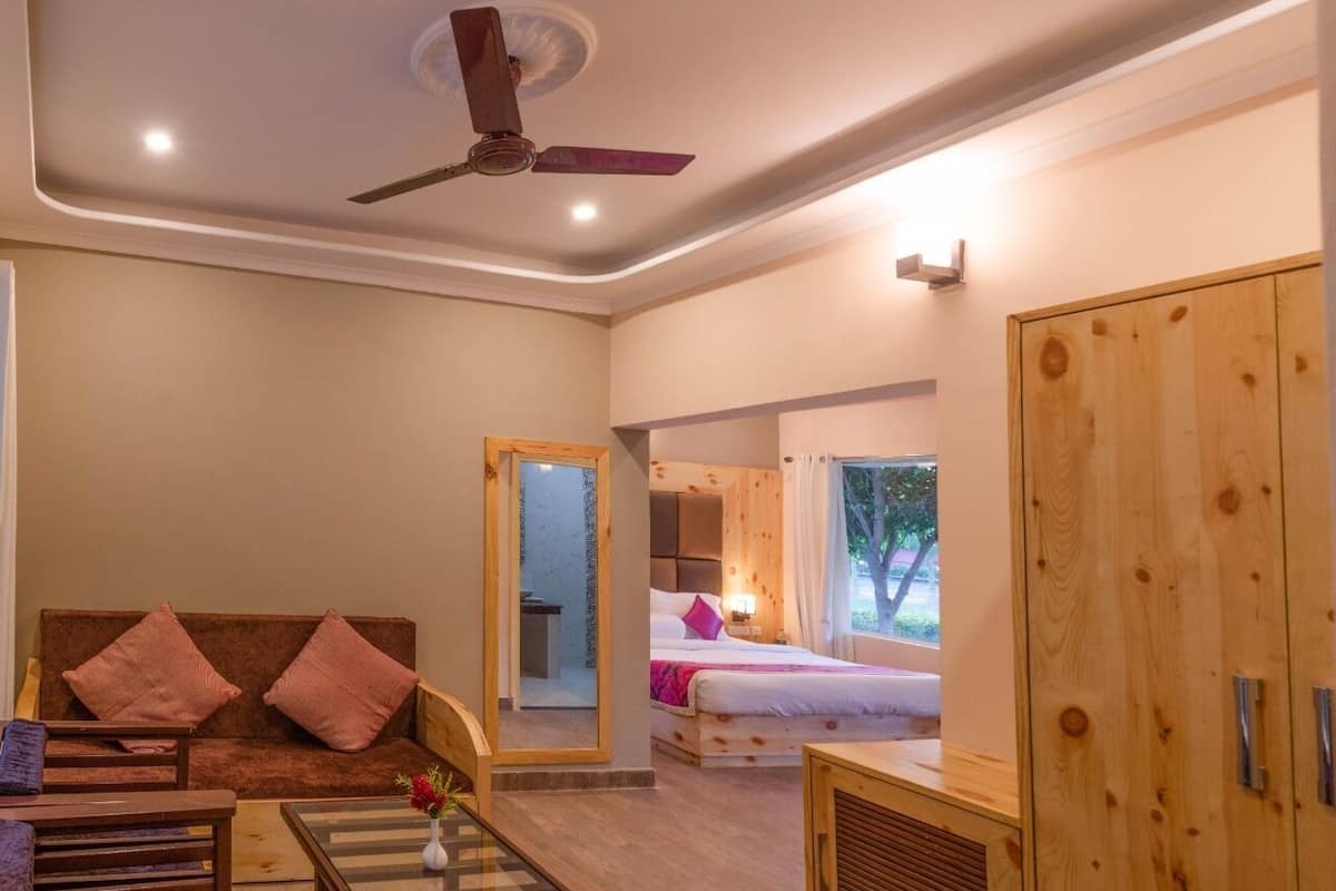 A hotel room with a bed, a sofa, a mirror, a ceiling fan, and a wardrobe.