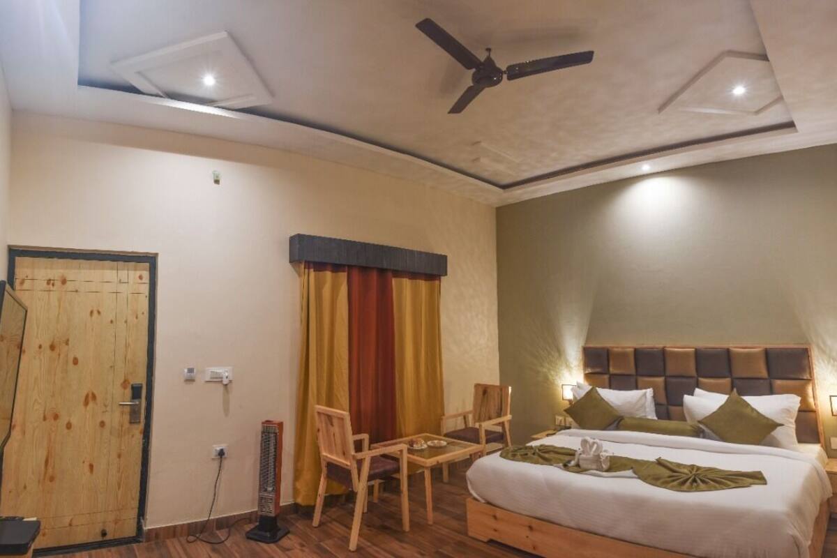 A hotel room with a bed, two chairs, a table, a ceiling fan, and a wooden door.