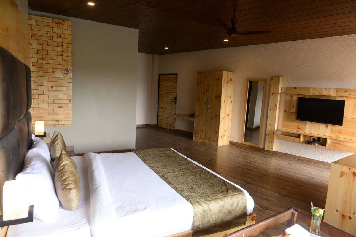 A bedroom with a bed, wooden wardrobe, and a TV mounted on the wall.