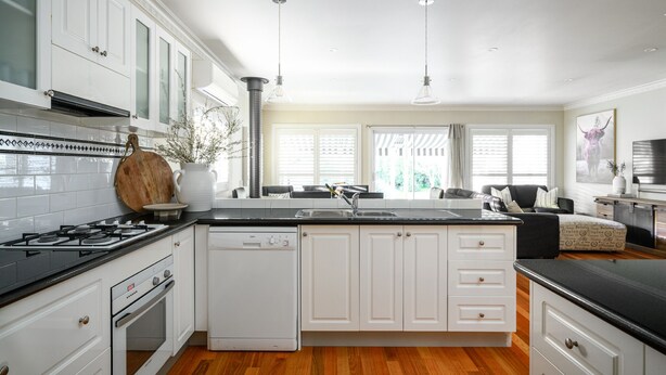 A modern kitchen with white cabinetry, a black countertop, a built-in dishwasher, and a gas stove. - Beautiful spacious home a short walk to town centre. (Bright)