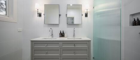 A modern bathroom with two sinks, a large mirror, and a glass shower enclosure.