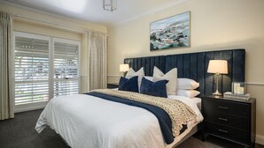 A neatly arranged bedroom with a large bed, two bedside tables, a painting, and a view through the window. - Beautiful spacious home a short walk to town centre. (Bright)