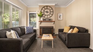 A living room with two dark sofas, a wooden coffee table, a fireplace, and a large wall clock. - Beautiful spacious home a short walk to town centre. (Bright)
