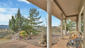 A covered patio with a view of a desert landscape, featuring a cactus, a large tree, and a chair. - Mountain Views | Pool Table | Spacious 4BR (Prescott)