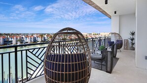 A balcony with a view of a marina, a spherical wicker chair, and a seating area with a rug and cushions.