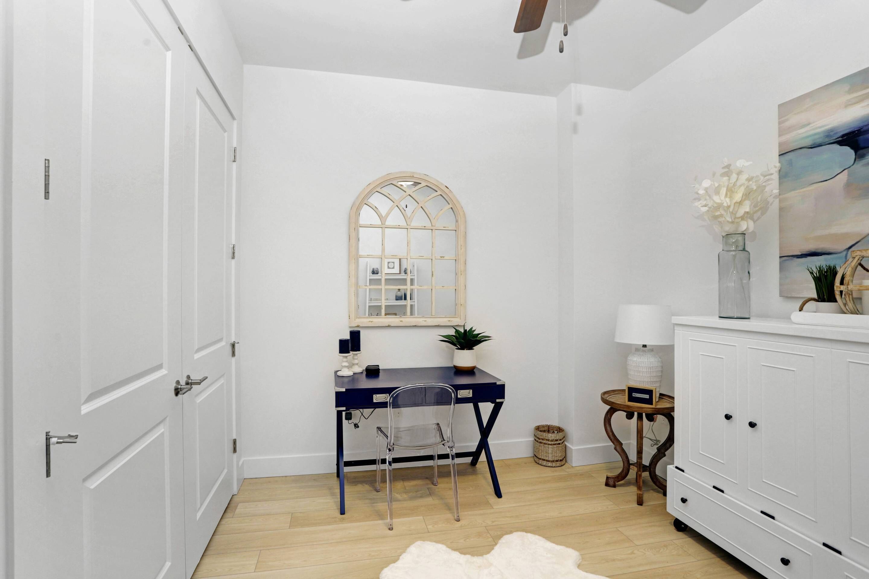 Ein Zimmer mit Schreibtisch, Stuhl, weißem Kleiderschrank und einem Gemälde an der Wand.