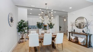 A modern dining area with a wooden table, white chairs, and a unique chandelier.
